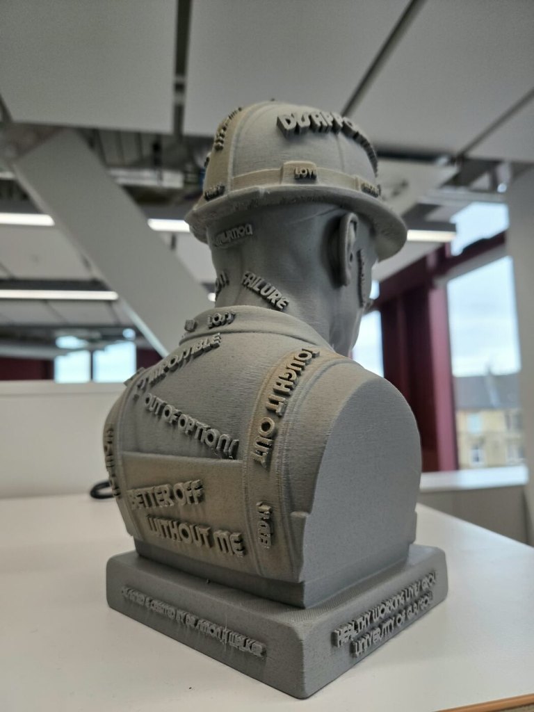 Rear view of the grey 3D-printed SOLVE Construction Bust, with raised words across the helmet and workwear