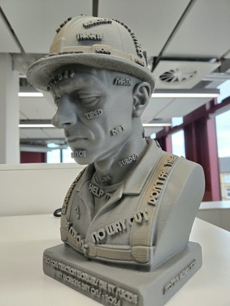 Grey 3D-printed SOLVE Construction Bust viewed from the side, showing raised words across the helmet, face and workwear