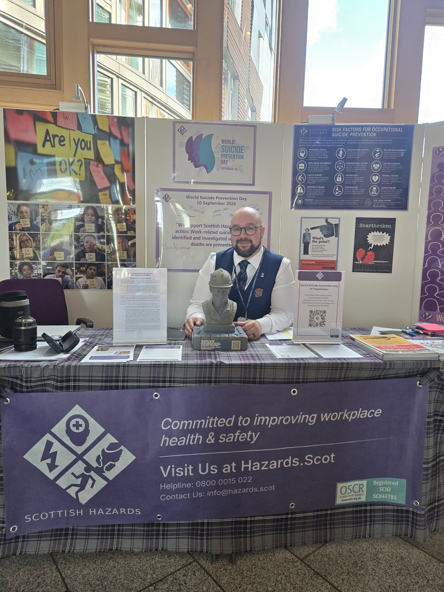 Dr Simon Harold Walker seated at the Scottish Hazards exhibition in the Scottish Parliament, with the construction bust on the table in front of him.